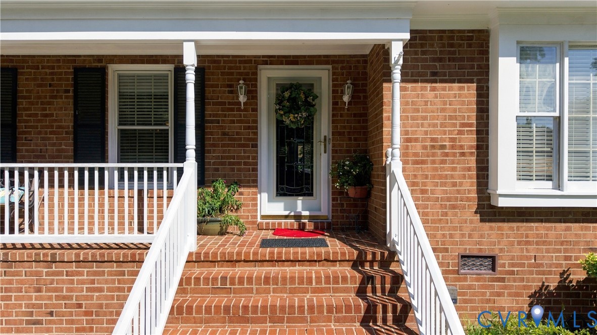 Brick exterior featuring a covered front porch, white railing, decorative shutters, and an inset front door with glass detailing