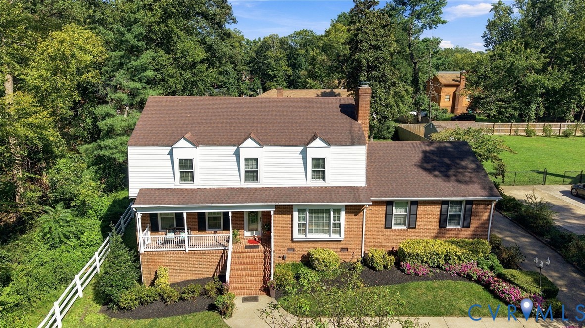 Two-story brick and siding exterior featuring a covered front porch, gabled roofline, multi-pane windows, and extensive mature landscaping