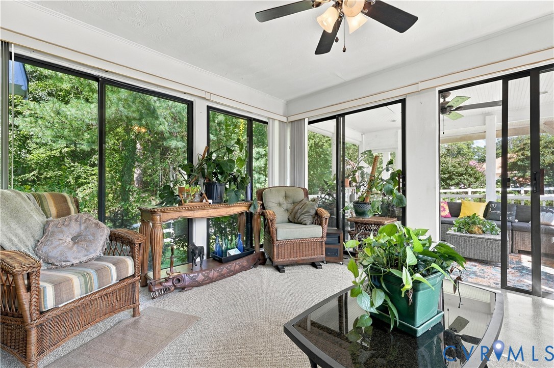 Enclosed sunroom featuring floor-to-ceiling glass sliding doors, neutral carpeting, and a ceiling fan with integrated lighting