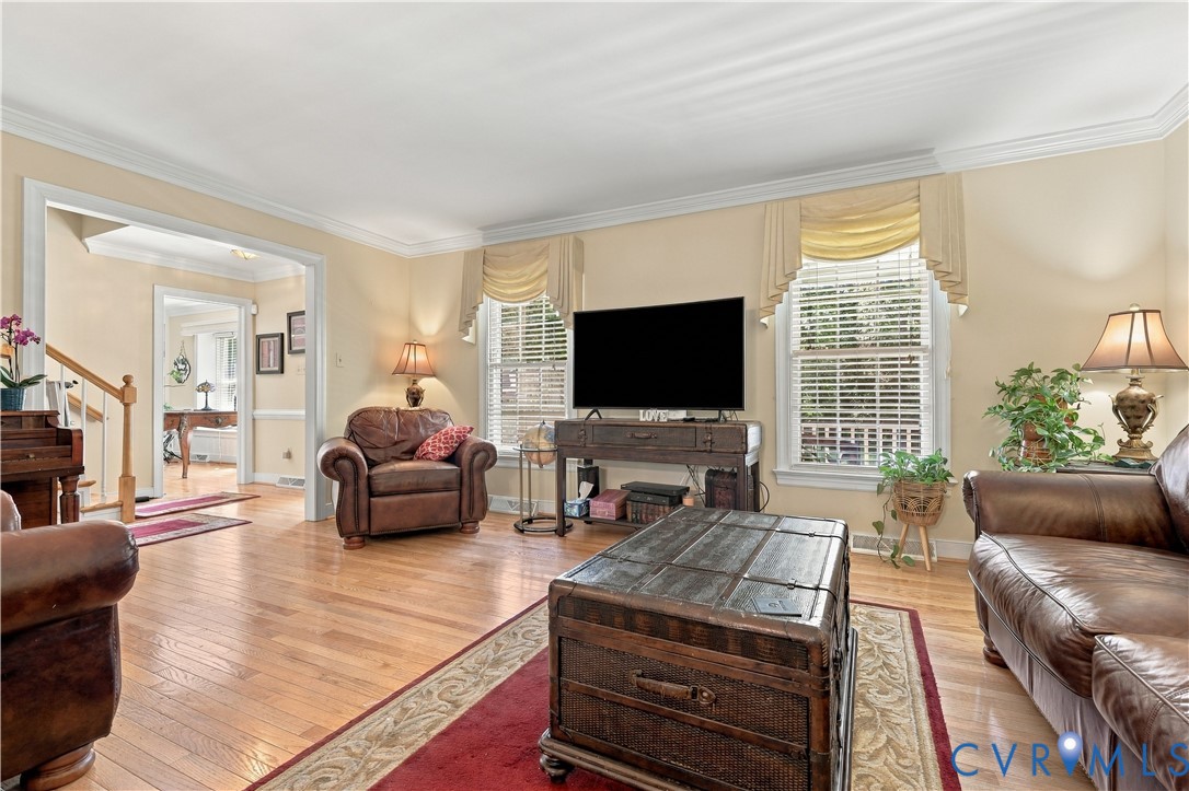 Living area featuring wood-finish flooring, crown molding, and dual windows with blinds