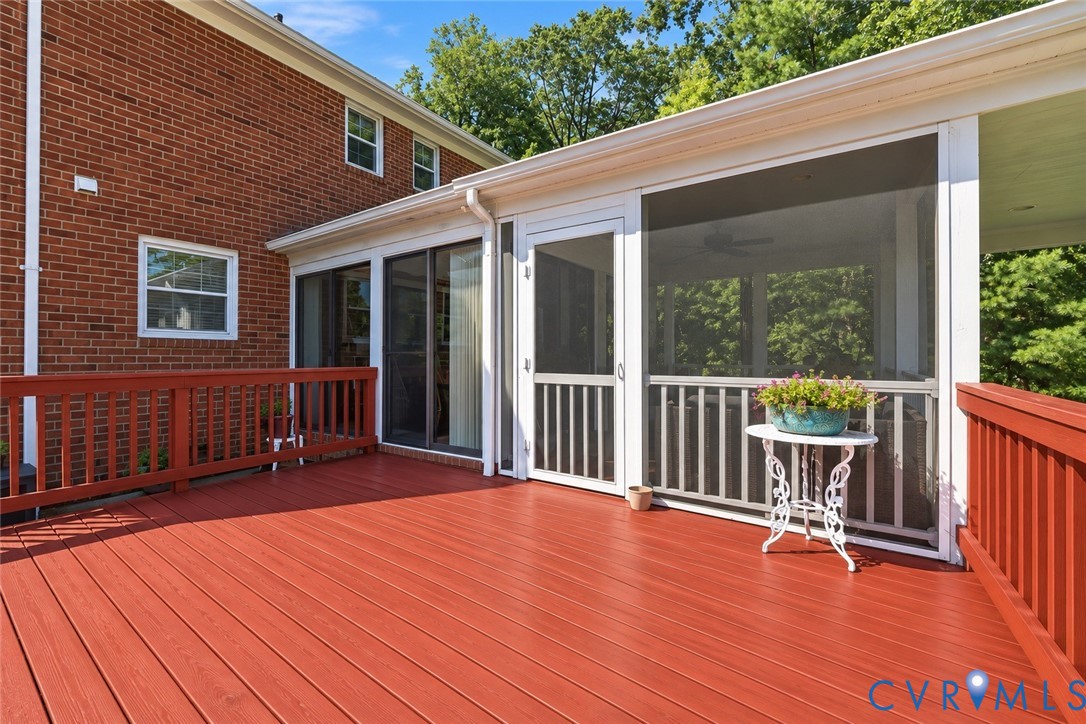 Expansive deck with wood-finish decking and perimeter railing, featuring a screened-in porch with white framing and sliding glass door access