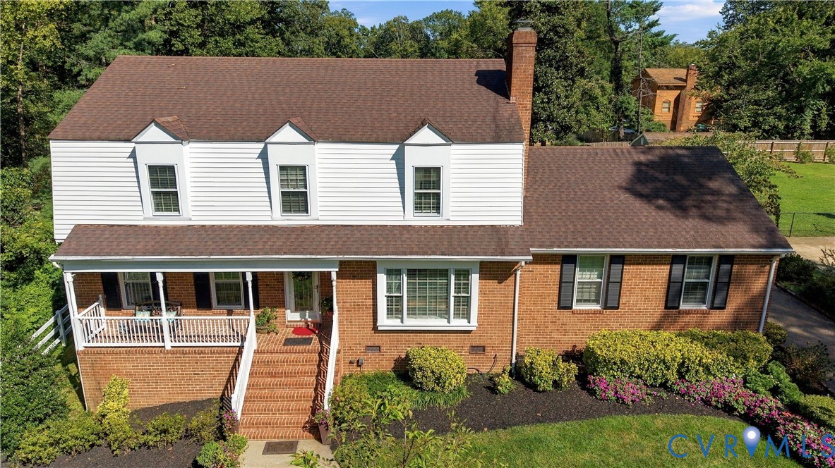 Two-story residence featuring a combination of brick and horizontal siding, a covered front porch with white railing, brick exterior staircase, three dormer windows, and a prominent exterior brick chimney