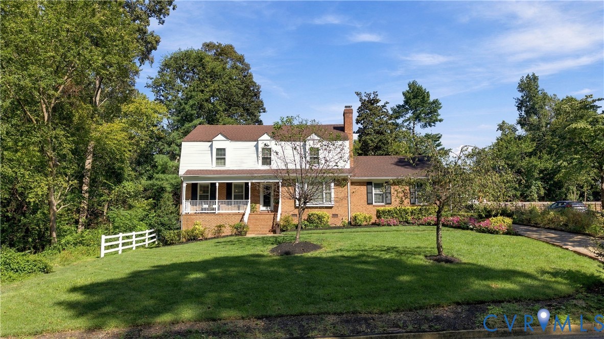 Two-story residence featuring a brick and siding exterior, a front-facing covered porch, a brick chimney, and a multi-gabled roofline, set on a manicured lot with white split-rail fencing