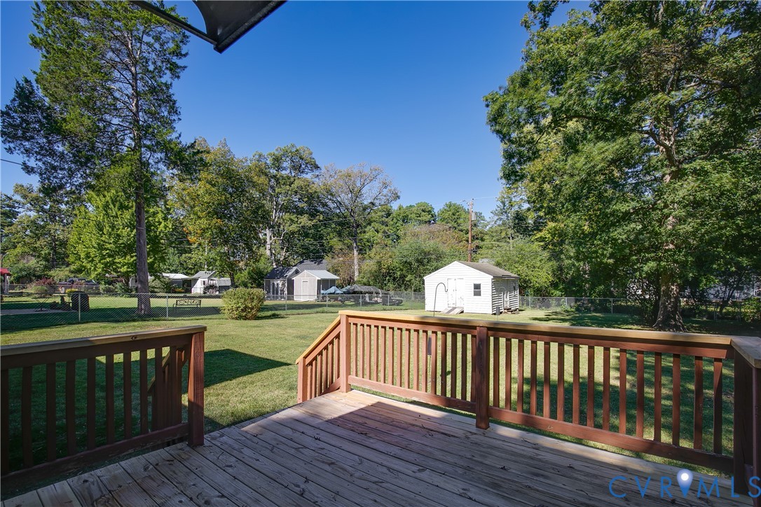 Elevated wood deck featuring vertical wood balusters and stairs leading to a spacious lawn, chain-link perimeter fencing, and a detached storage structure