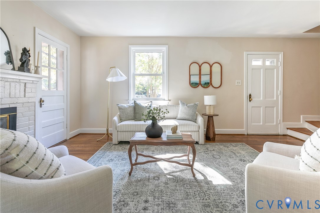 Living room featuring wood-finish flooring, a painted brick fireplace, multi-pane glass doors, and a double-hung window