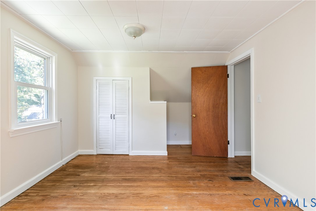 Interior space featuring wood-finish flooring, white louvered closet doors, a natural-finish wood door, and a flush-mount ceiling fixture