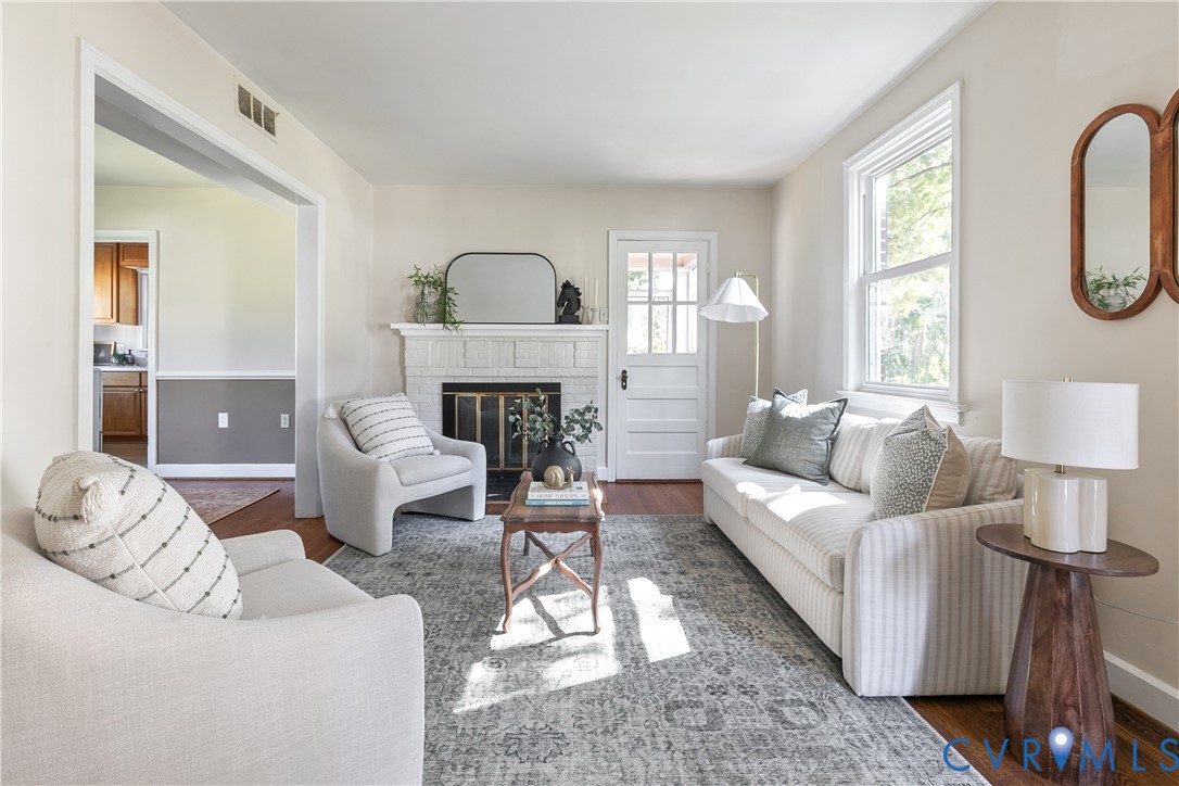 Living space featuring a brick fireplace, wood-finish flooring, multi-pane window, and an exterior door with glass detailing Living space featuring a brick fireplace, wood-finish flooring, multi-pane window, and an exterior door with glass detailing