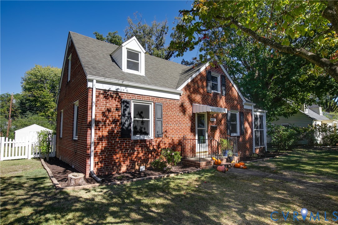 Red brick exterior featuring a steep-pitched roof, dual dormer windows, shutter-framed window casings, and a metal-awning front entry Red brick exterior featuring a steep-pitched roof, dual dormer windows, shutter-framed window casings, and a metal-awning front entry