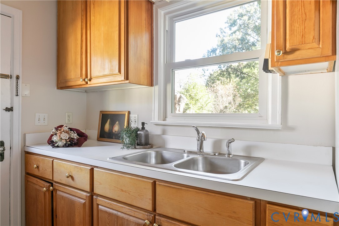 Natural wood cabinetry, white solid-surface countertop, dual-basin stainless steel sink, and integrated metal faucet hardware
