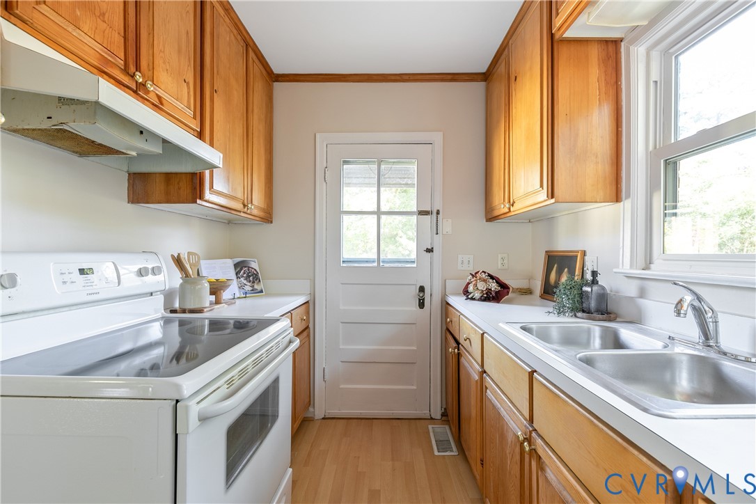 Kitchen featuring wood cabinetry, white countertops, double basin stainless steel sink, electric range, and wood-finish flooring