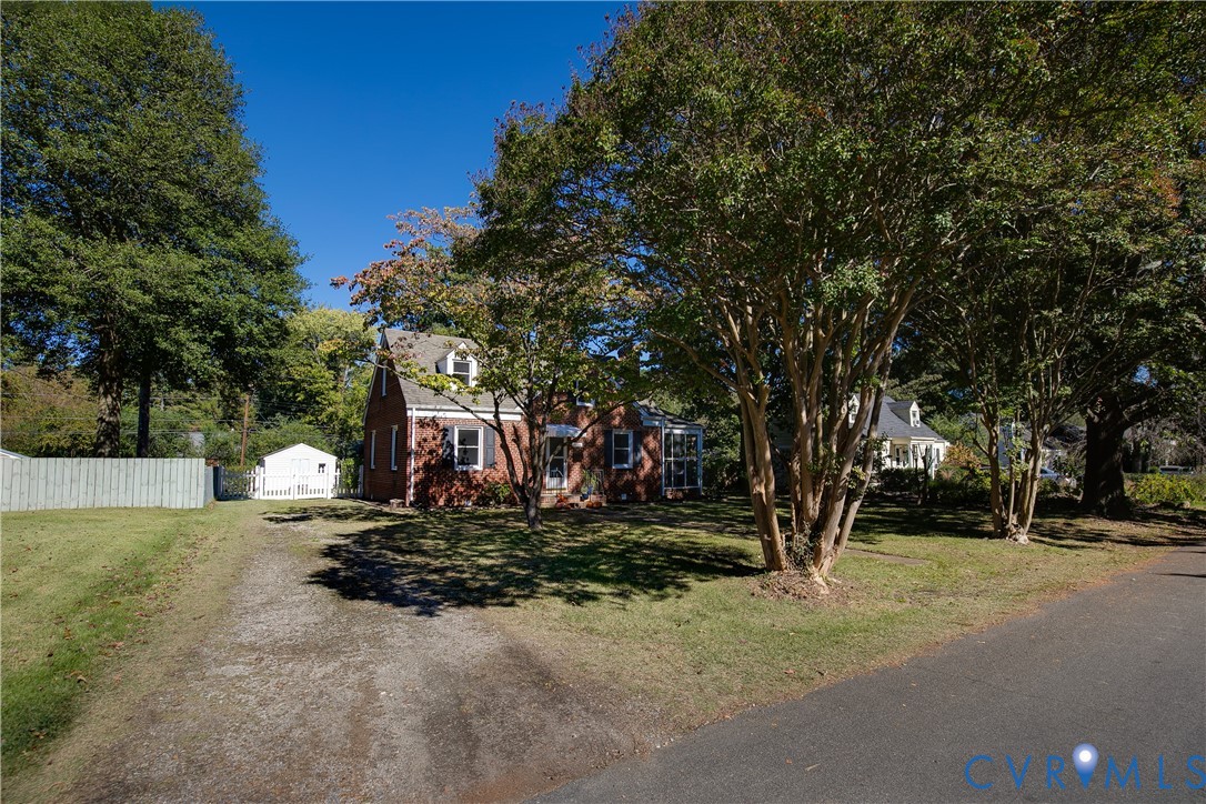 Brick exterior featuring dormer windows, a pitched shingle roof, mature landscaping, and a detached storage structure Brick exterior featuring dormer windows, a pitched shingle roof, mature landscaping, and a detached storage structure