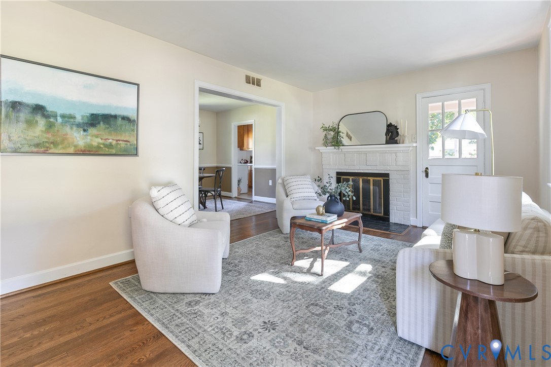 Living area featuring wood-finish flooring, a painted brick fireplace with a mantel, and a multi-lite glass panel door Living area featuring wood-finish flooring, a painted brick fireplace with a mantel, and a multi-lite glass panel door