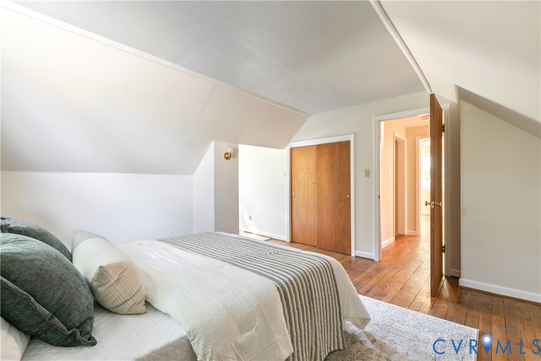 Sloped ceiling architecture featuring wood-finish flooring, built-in wooden closet doors, and wall-mounted light fixture