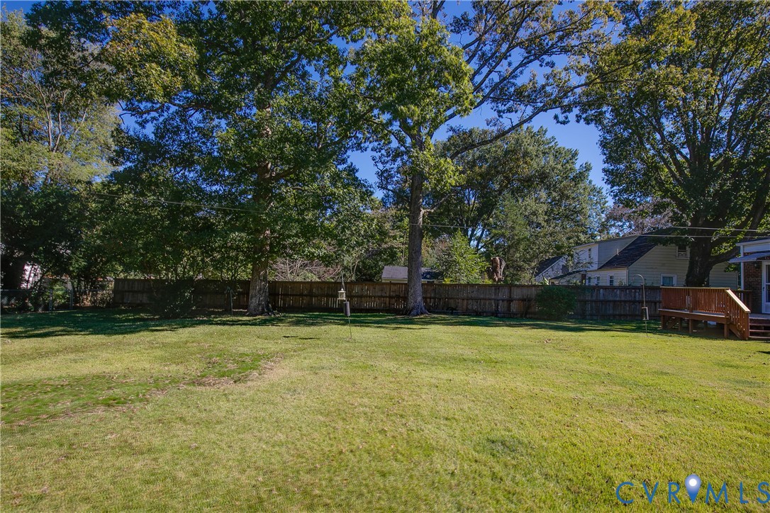 Expansive backyard featuring a fenced perimeter, mature trees, and a wooden deck