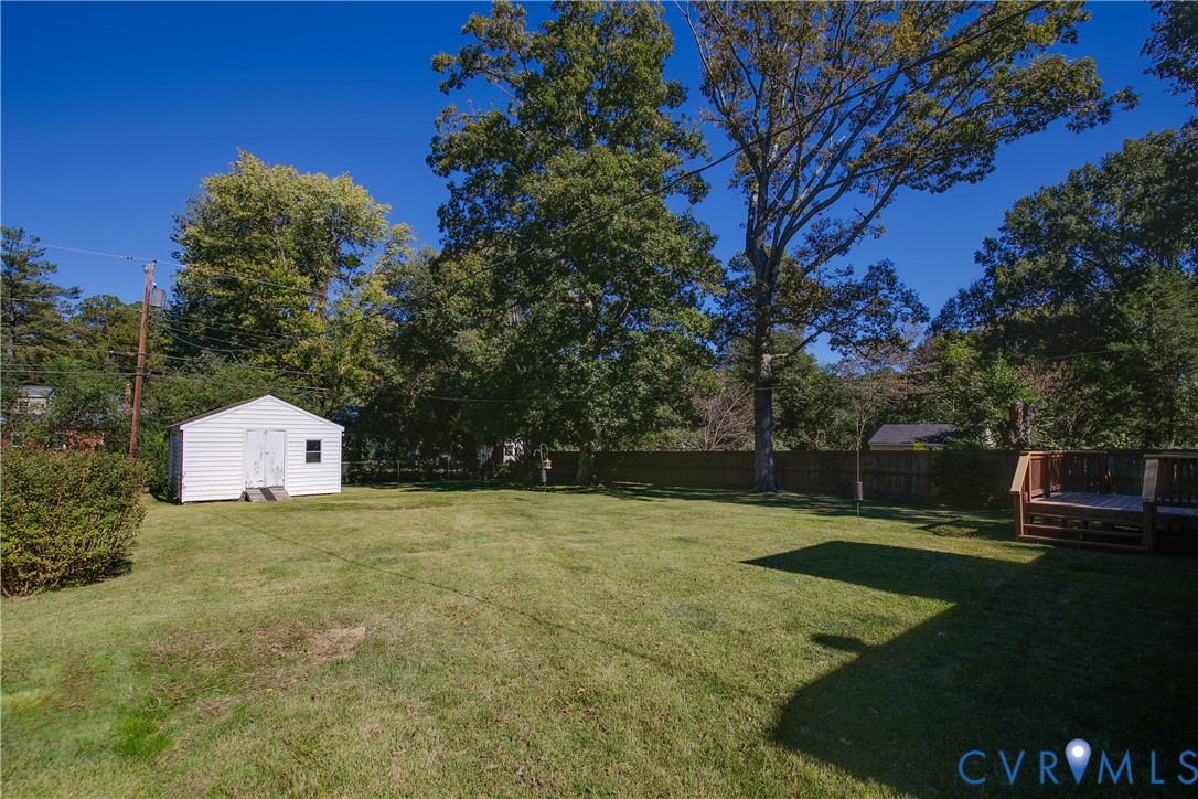Expansive backyard featuring a lawn, mature trees, wood-style fencing, an elevated wooden deck, and a detached storage structure