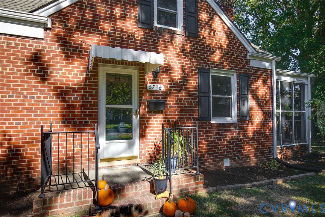 Red brick exterior featuring dark shutters, a decorative metal door canopy, and a glass-paneled storm door with metal railings Red brick exterior featuring dark shutters, a decorative metal door canopy, and a glass-paneled storm door with metal railings