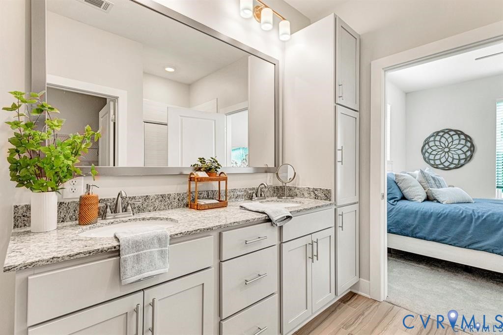 Double vanity featuring stone countertops, integrated cabinetry with brushed hardware, a large-format mirror, and three-light glass fixture