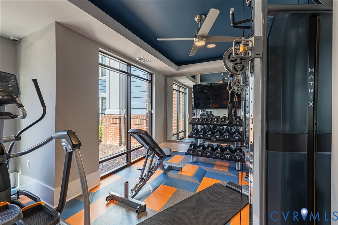 Fitness center featuring floor-to-ceiling windows, mirrored wall, patterned synthetic flooring, and a recessed ceiling with a central fan