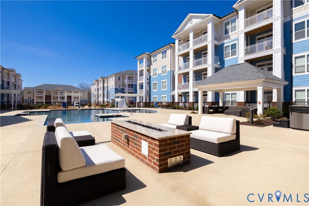 Outdoor community space featuring a swimming pool, covered pavilion with columns, brick-constructed fire pit with a stone top, and expansive concrete decking