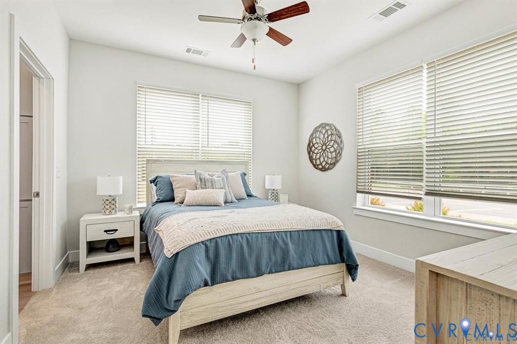 Neutral-toned room featuring neutral carpeting, a ceiling fan with integrated lighting, dual windows with blinds, and light-toned wall finishes