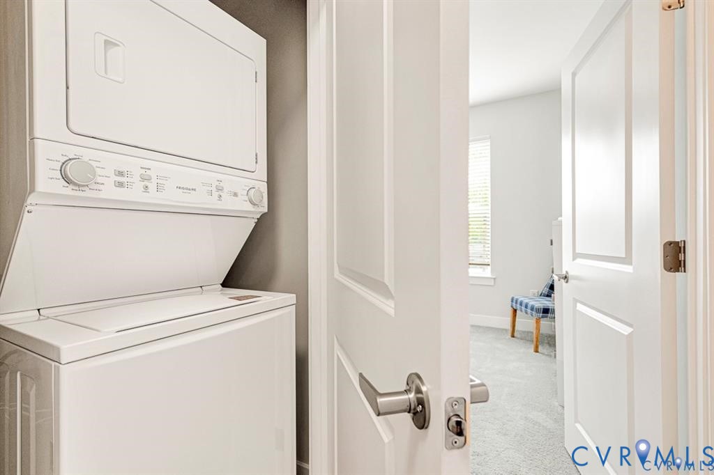 Stacked laundry unit featuring white appliances, recessed into a dedicated alcove with neutral-tone wall surfacing, accessible via a solid-core interior door with a brushed nickel lever handle