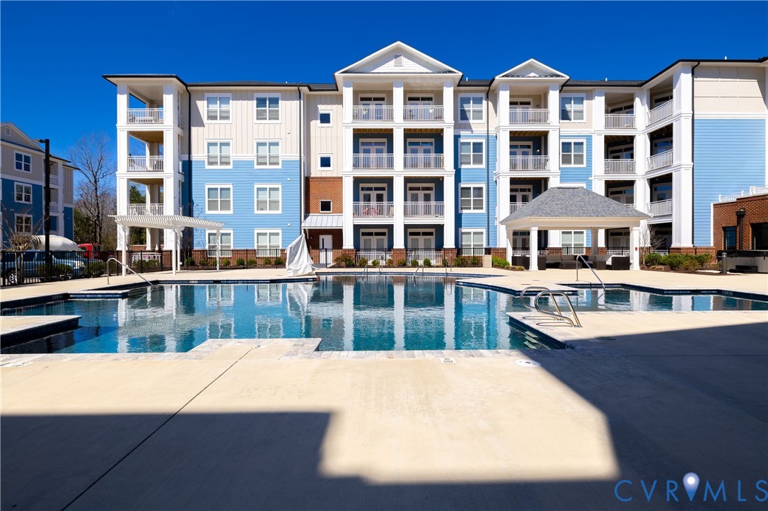 Swimming pool with concrete decking, featuring a covered gazebo, structural columns, and multi-story building facade with private balconies