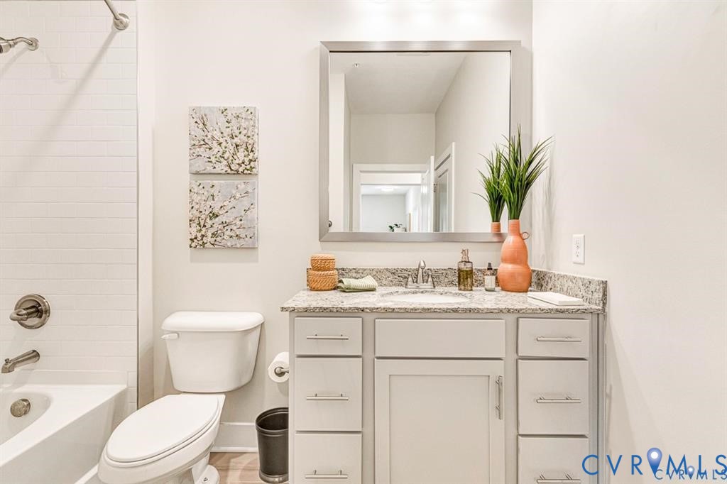 Bathroom featuring a vanity with neutral-toned cabinetry, stone-finish countertop, undermount sink, and a large rectangular mirror, complemented by a white subway-tile shower surround