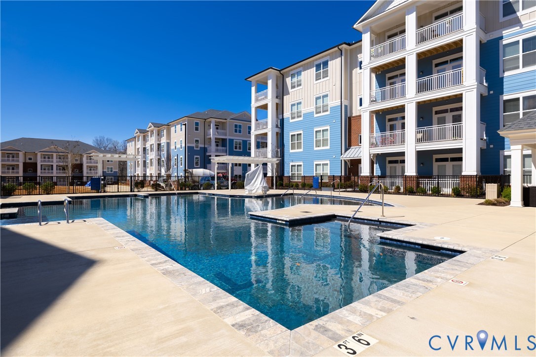 Outdoor swimming pool featuring a stone-tile coping, concrete deck, metal handrails, and a dedicated spa area