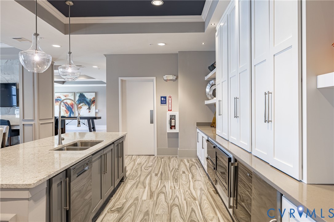 Kitchen featuring a center island with a dual-basin sink, quartz countertops, floor-to-ceiling white cabinetry, wood-finish flooring, and glass pendant lighting Kitchen featuring a center island with a dual-basin sink, quartz countertops, floor-to-ceiling white cabinetry, wood-finish flooring, and glass pendant lighting
