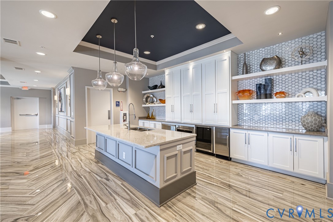 Kitchen island featuring a stone countertop and undermount sink, complemented by white cabinetry, glass-tile backsplash, built-in stainless steel appliances, and large-format tile flooring Kitchen island featuring a stone countertop and undermount sink, complemented by white cabinetry, glass-tile backsplash, built-in stainless steel appliances, and large-format tile flooring