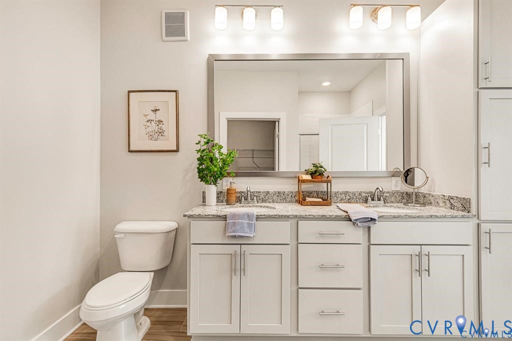 Double vanity featuring light cabinetry, stone-finish countertops with dual undermount sinks, a large rectangular mirror, and dual wall-mounted light fixtures