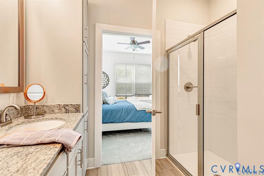 Bathroom featuring stone-surface countertop, integrated oval sink, tall built-in cabinetry, and a glass-enclosed shower with tiled surround