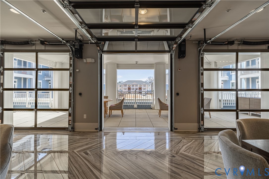 Open-concept space featuring retractable glass garage-style doors, high-gloss stone-finish flooring in a chevron pattern, and an exterior balcony with tile surfacing Open-concept space featuring retractable glass garage-style doors, high-gloss stone-finish flooring in a chevron pattern, and an exterior balcony with tile surfacing