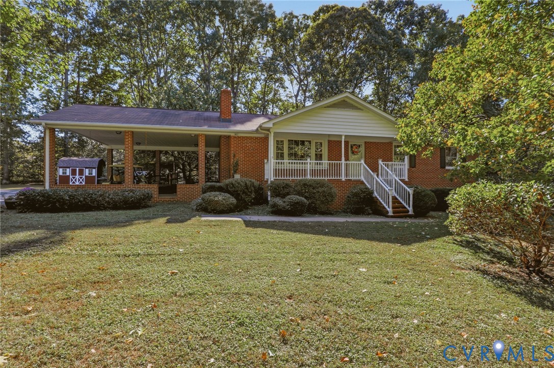Brick exterior residence featuring an attached carport, covered front porch with white railing, and mature landscaping