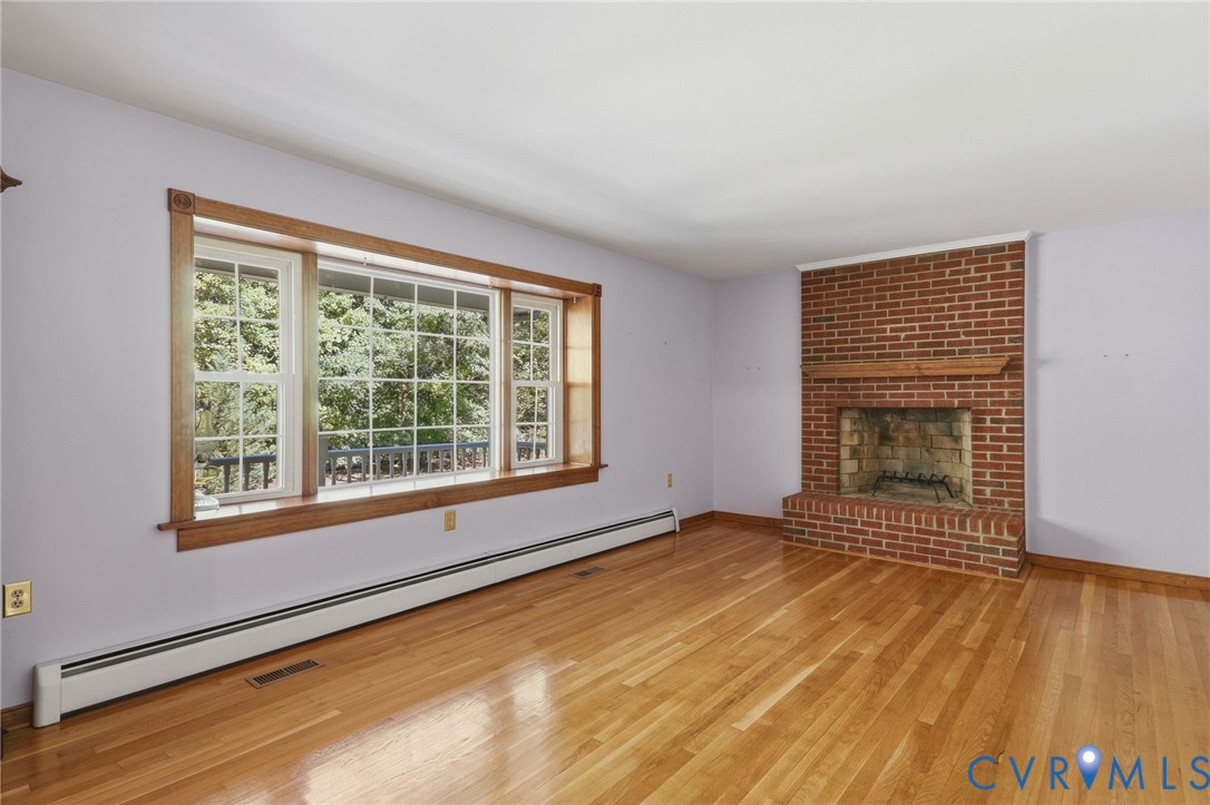 Hardwood flooring, wood-framed bay window, and red brick fireplace featuring a wood mantel