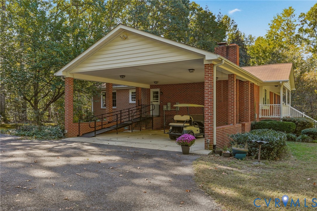 Brick exterior with a covered carport, built-in masonry chimney, and metal access ramp