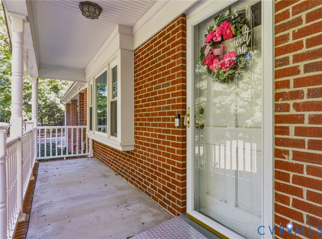 Covered front porch featuring red brick exterior wall, white wood-finish columns, white balustrade railing, and a full-light glass storm door