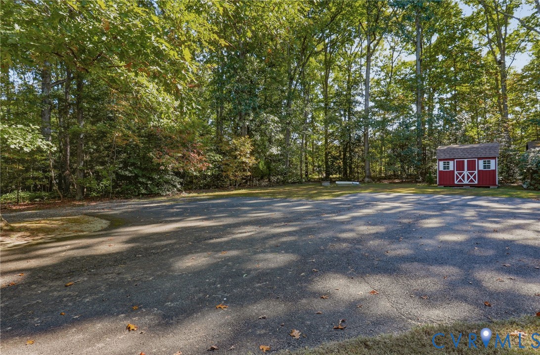 Expansive paved area featuring a standalone storage structure, bordered by mature trees and dense woodland