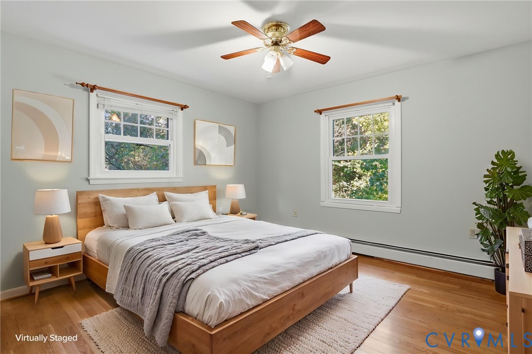 Bedroom featuring wood-finish flooring, two multi-pane windows with white trim, and a ceiling-mounted light fixture with a fan