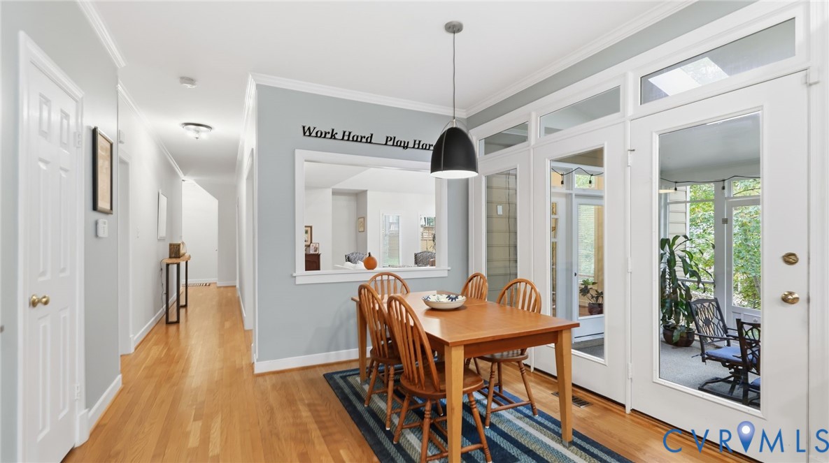 Dining area featuring wood-finish flooring, a contemporary pendant light fixture, a pass-through wall opening, and multi-pane glass doors with transom windows