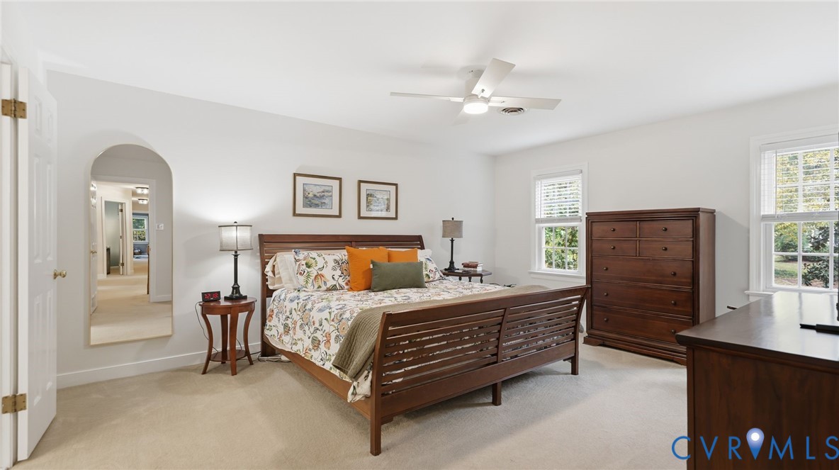 Room featuring neutral carpeting, an arched entryway, a ceiling fan with integrated lighting, and multi-pane windows