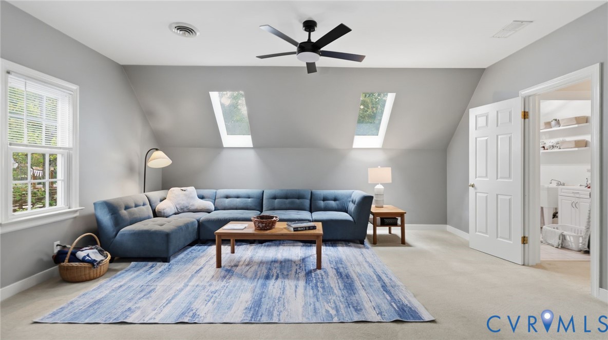 Room with vaulted ceilings, two skylights, wall-to-wall carpeting, modern matte black ceiling fan, and access to a secondary space through a panel door