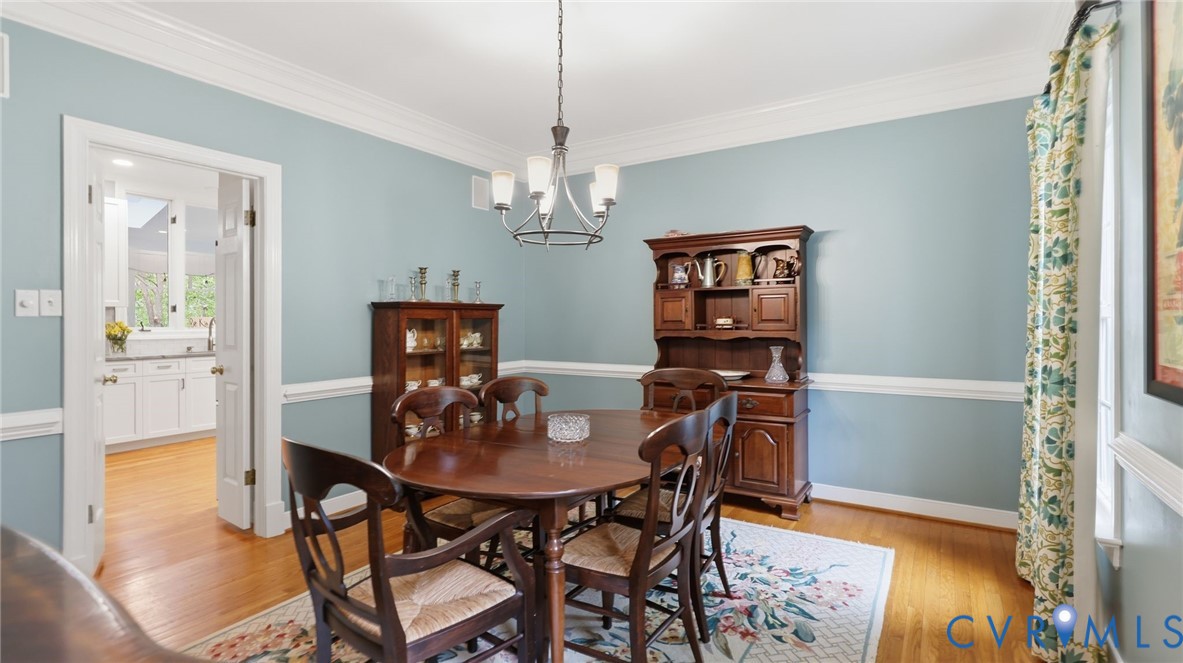Dining area featuring crown molding, chair rail trim, wood-finish flooring, and a multi-arm chandelier