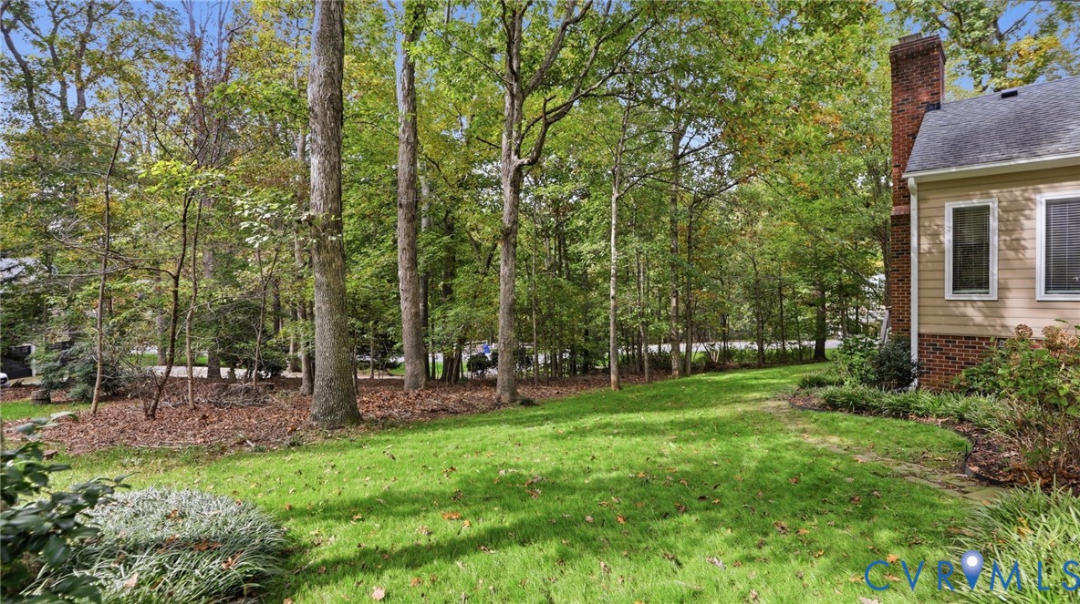 Expansive yard featuring a manicured lawn, mature trees, and a brick exterior chimney
