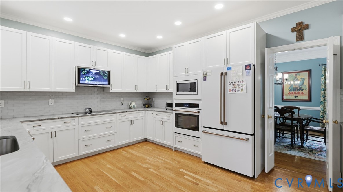 Kitchen featuring white shaker-style cabinetry, light stone-finish countertops, subway tile backsplash, recessed lighting, and built-in stainless steel double wall ovens