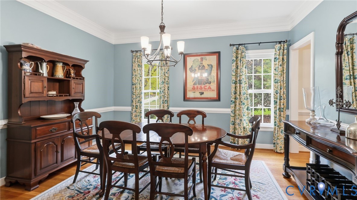 Dining room featuring crown molding, chair rail trim, wood-finish flooring, and a multi-light chandelier