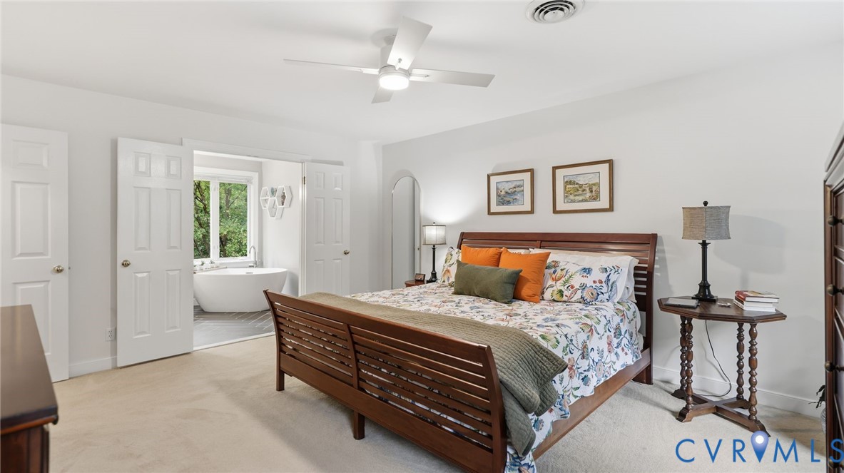 Bedroom featuring neutral carpeting, a white ceiling fan with integrated lighting, and double doors opening to a space containing a freestanding soaking tub