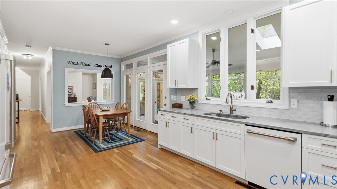 Kitchen featuring white cabinetry, stone countertops, a subway tile backsplash, stainless steel sink hardware, and wood-finish flooring