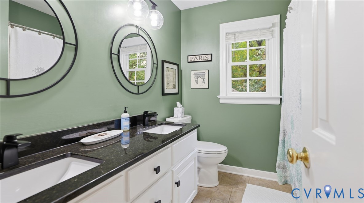 Dual-sink vanity with dark stone countertop, matte black fixtures, circular mirrors, and multi-pane window