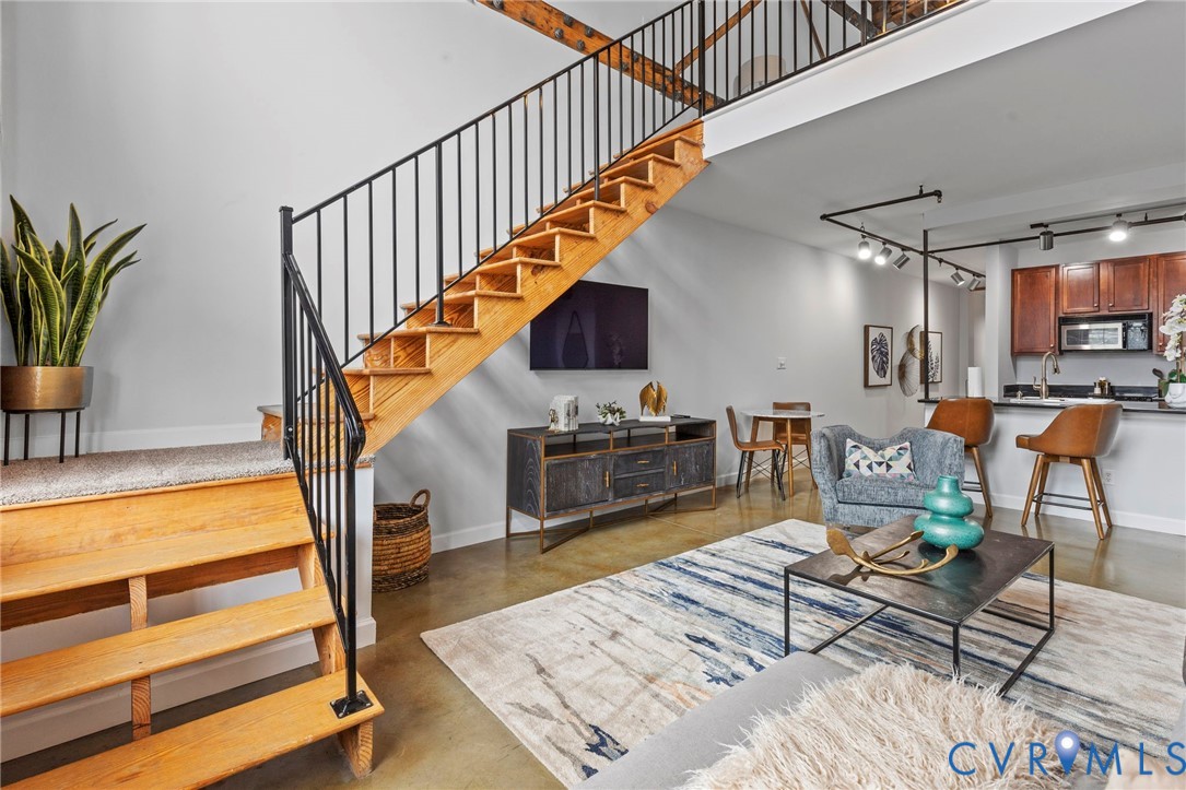 Open-concept interior featuring wood-tread staircase with black metal railing, soaring vaulted ceilings, polished concrete flooring, and industrial-style track lighting